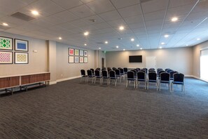 A conference room with a carpeted floor, a row of chairs, a wooden cabinet, and framed artwork on the wall.