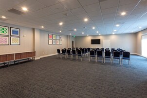 Un salón de conferencias con piso alfombrado, una fila de sillas, un armario de madera y obras de arte enmarcadas en la pared.