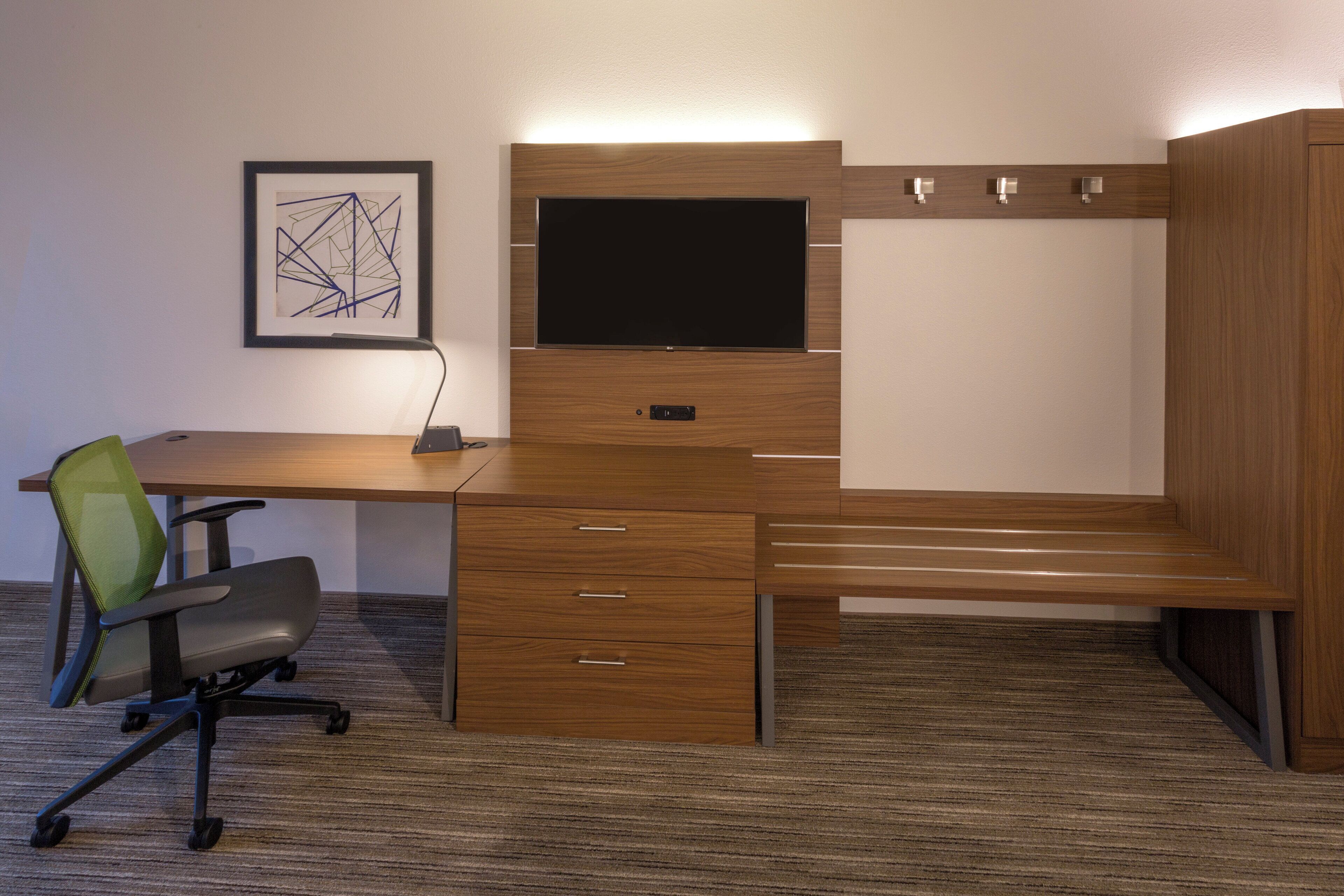 A modern office desk with a flat-screen monitor, a chair, and a framed abstract artwork on the wall.
