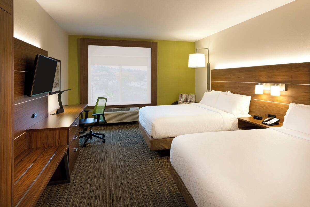 A hotel room with two beds, a desk with a chair, a television, a window with a view, and a bedside lamp.