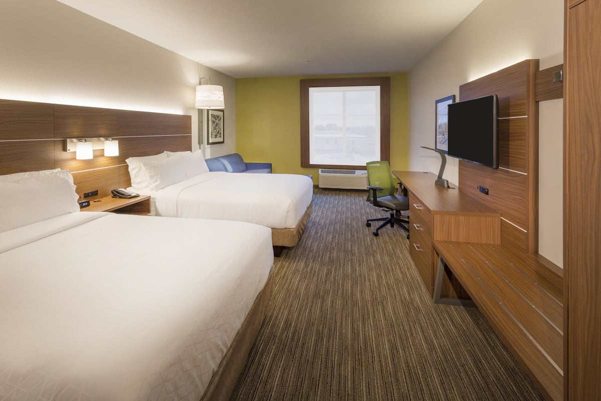 A hotel room with two beds, a desk with a flat-screen TV, a chair, and a window with a view.