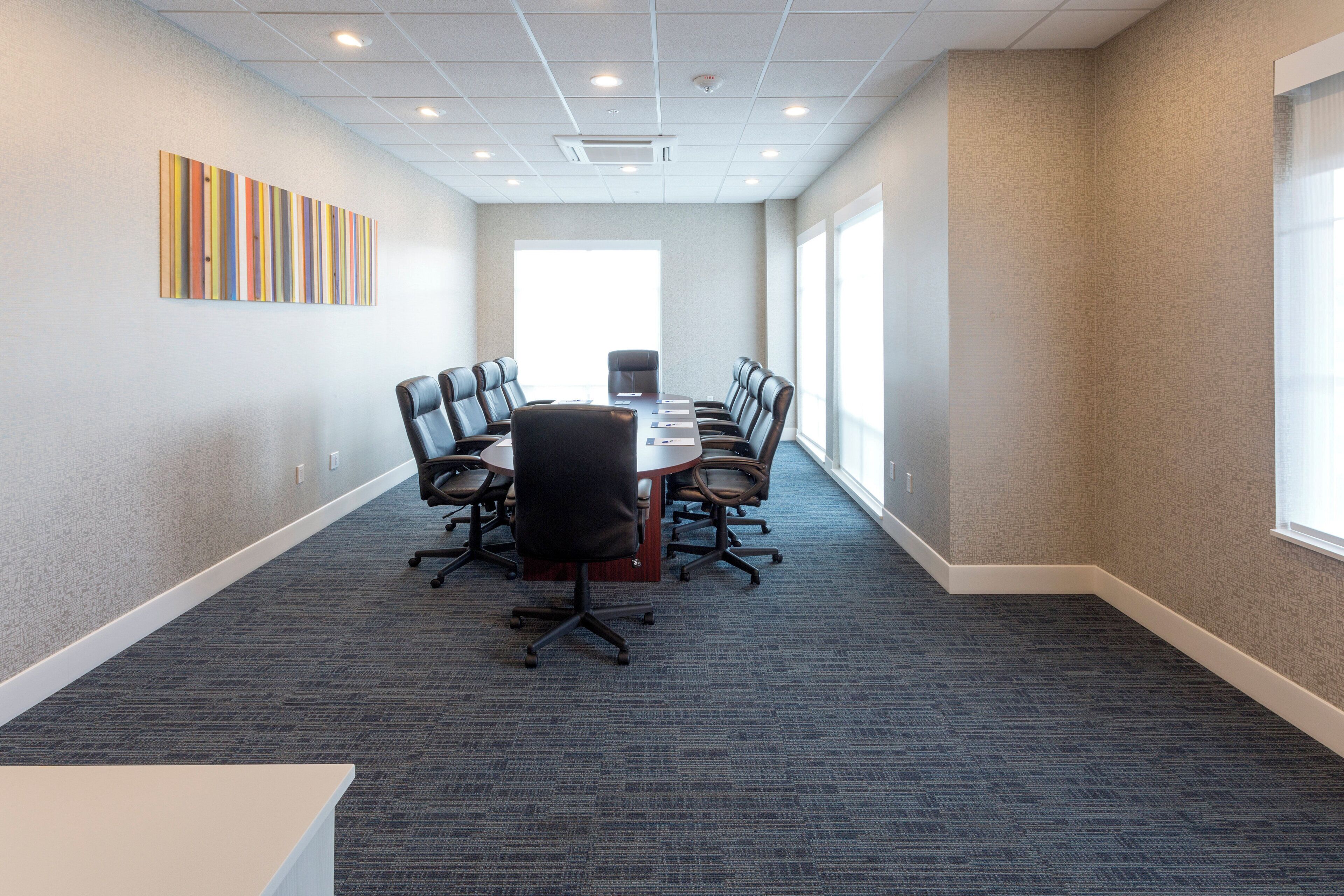A conference room with a long table, chairs, and a carpeted floor.