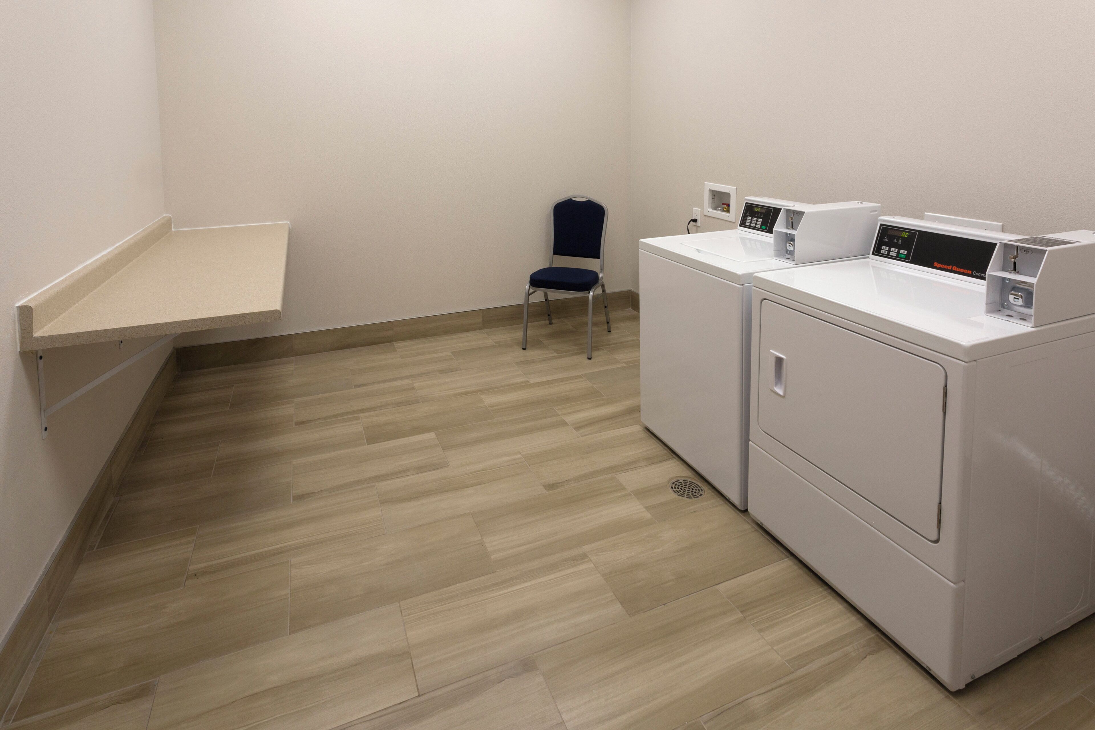 A laundry room with two washing machines, a chair, and a small shelf.