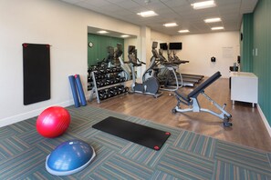 A fitness center with exercise equipment, a wall-mounted clock, and a reception desk. - Holiday Inn Express & Suites Seattle South - Tukwila by IHG (Tukwila)
