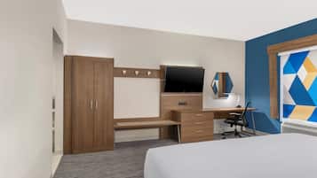 Una habitación de hotel con cama, escritorio con computadora, televisor y armario.