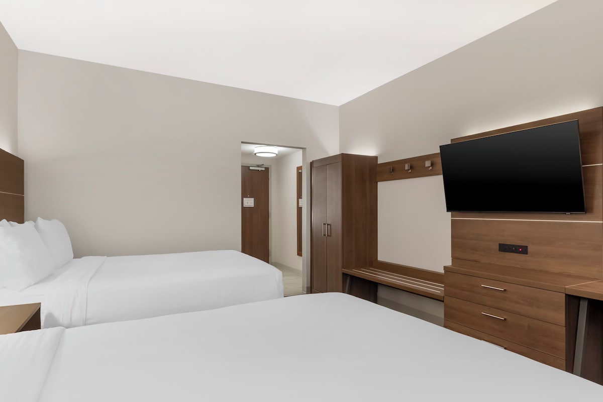 Une chambre d’hôtel avec deux lits, une télévision, des meubles en bois et un miroir.