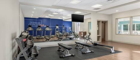 Une salle de sport équipée de matériel d’exercice, avec un grand miroir et un téléviseur fixé au mur.
