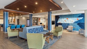 A modern hotel lobby with a blue and white patterned sofa, green armchairs, a small round table, and a map mural on the wall. - Holiday Inn Express Spring Hill by IHG (Spring Hill)