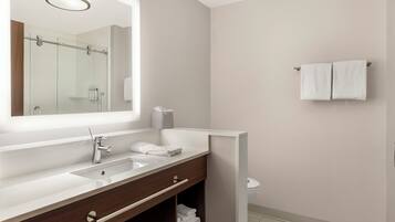 A modern bathroom with a large mirror, two sinks, a towel rack, and a toilet.