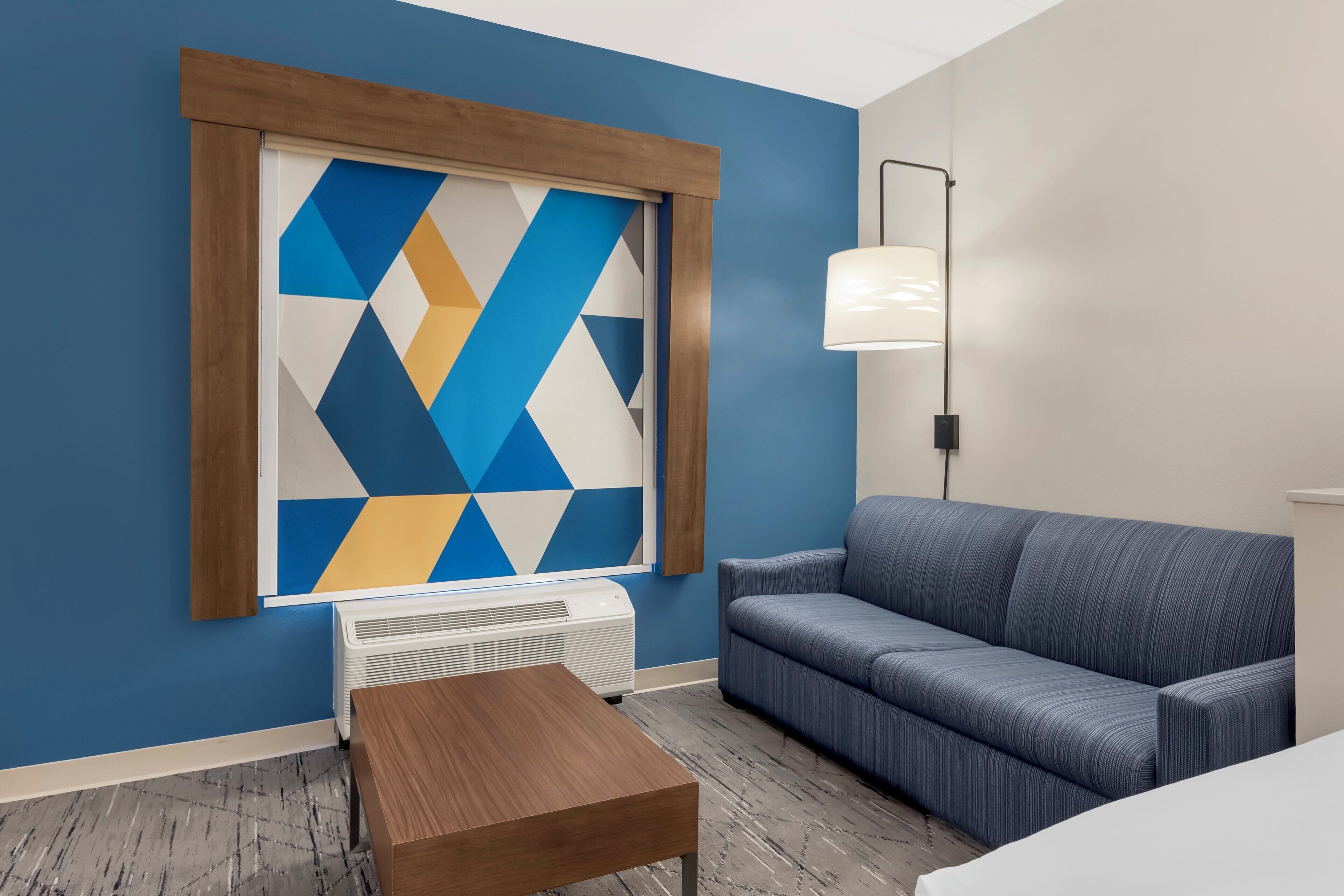 Une pièce avec un mur bleu, une œuvre d’art aux motifs géométriques, un canapé bleu, une table en bois et un lampadaire.