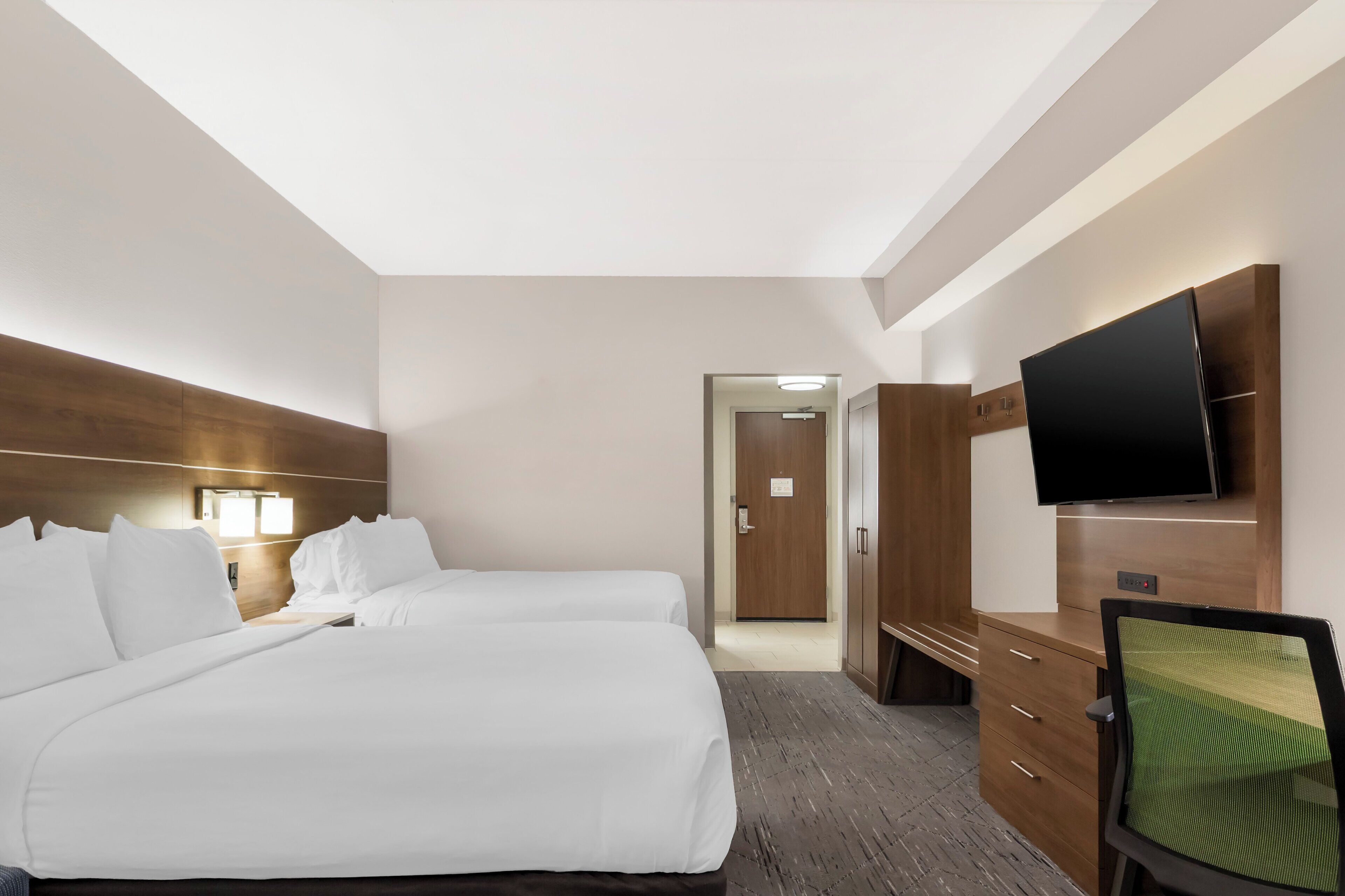 A hotel room with two beds, a desk, a chair, a television, and a wardrobe.