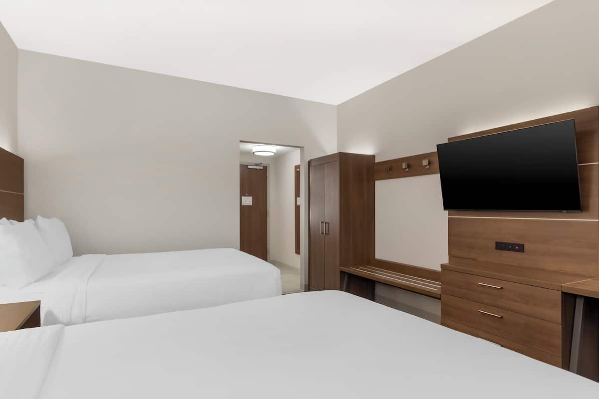A hotel room with two beds, a TV, wooden furniture, and a mirror.