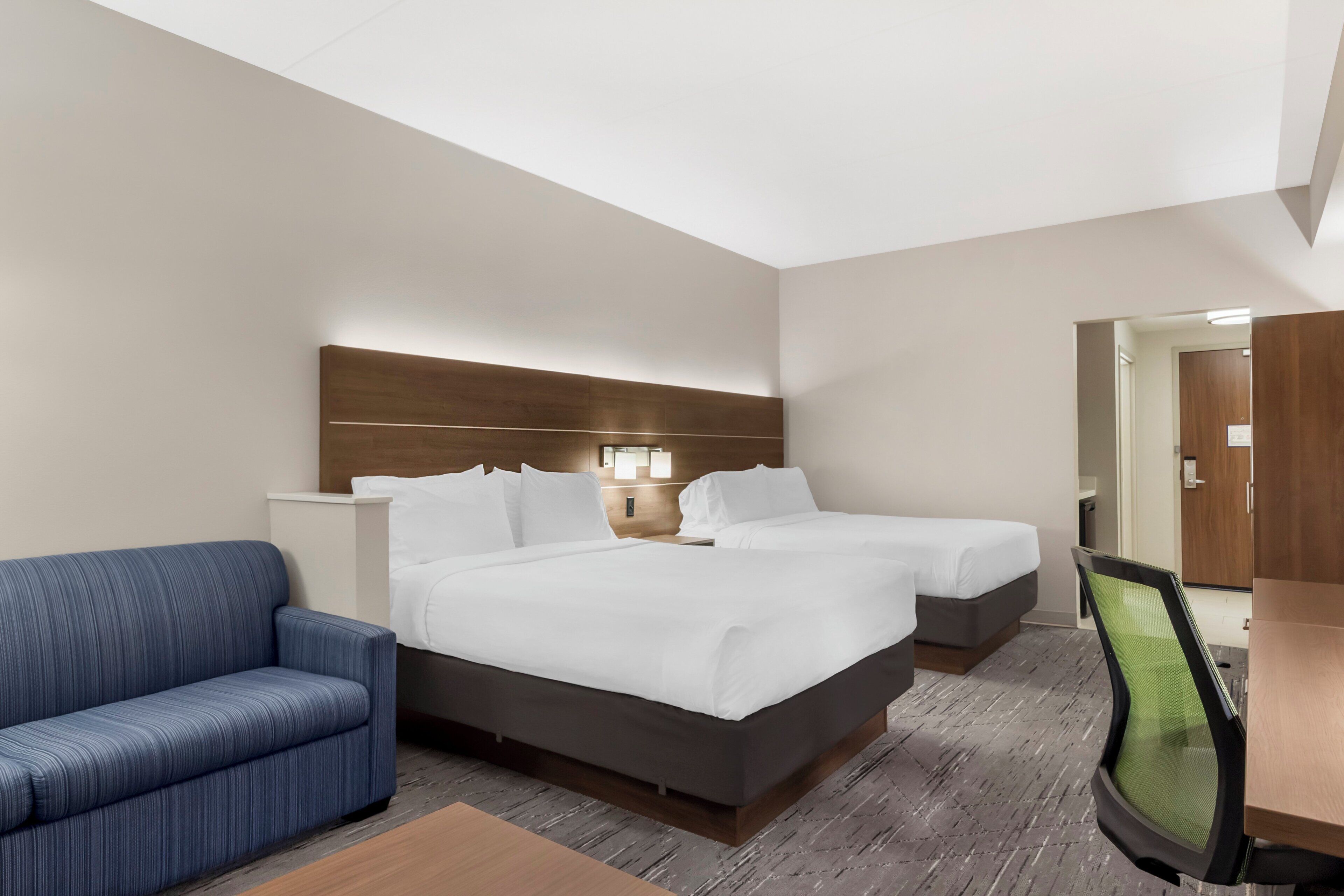 A hotel room with a large bed, a smaller bed, a sofa, a desk, and a chair.