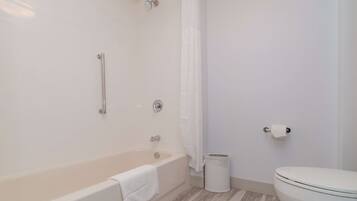 A bathroom with a bathtub, a toilet, and a trash can.