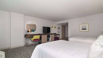 Habitación de hotel con dos camas, un escritorio con silla, televisión y espejo.
