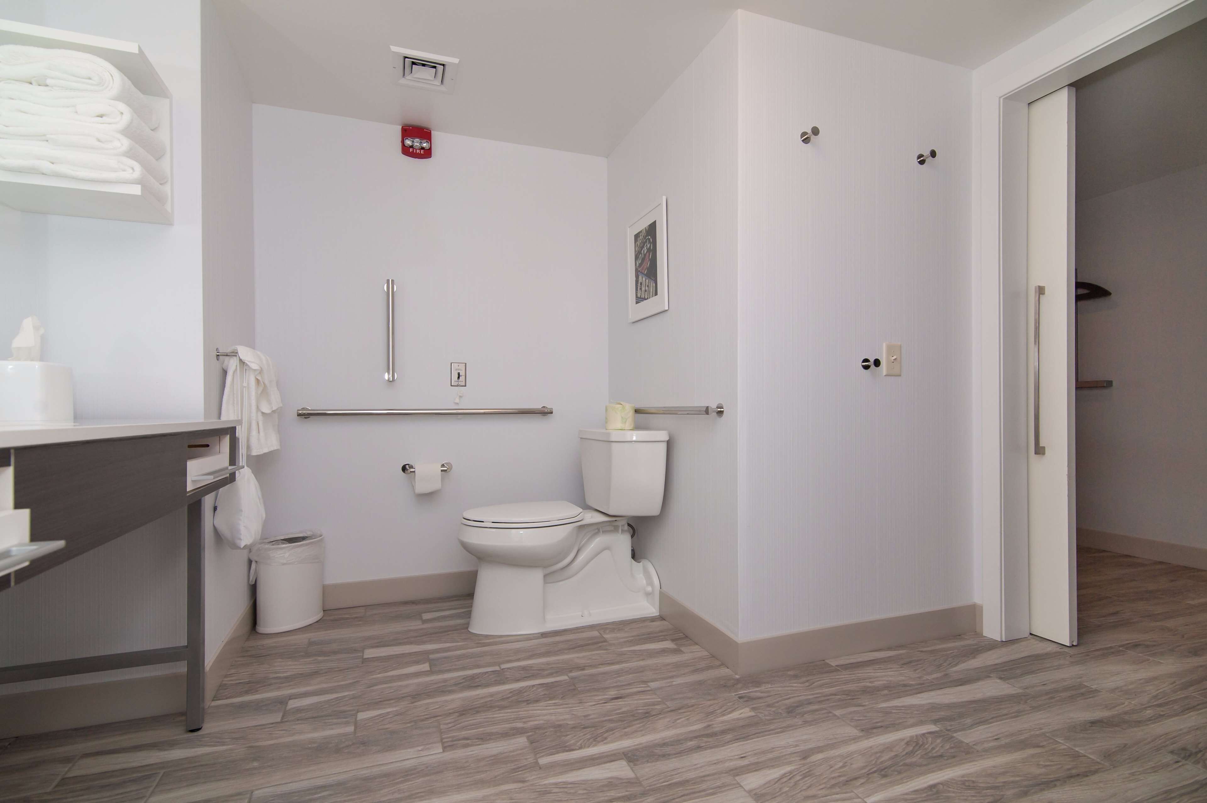 Un baño moderno con inodoro, barras de apoyo, toallero y un cubo de basura.