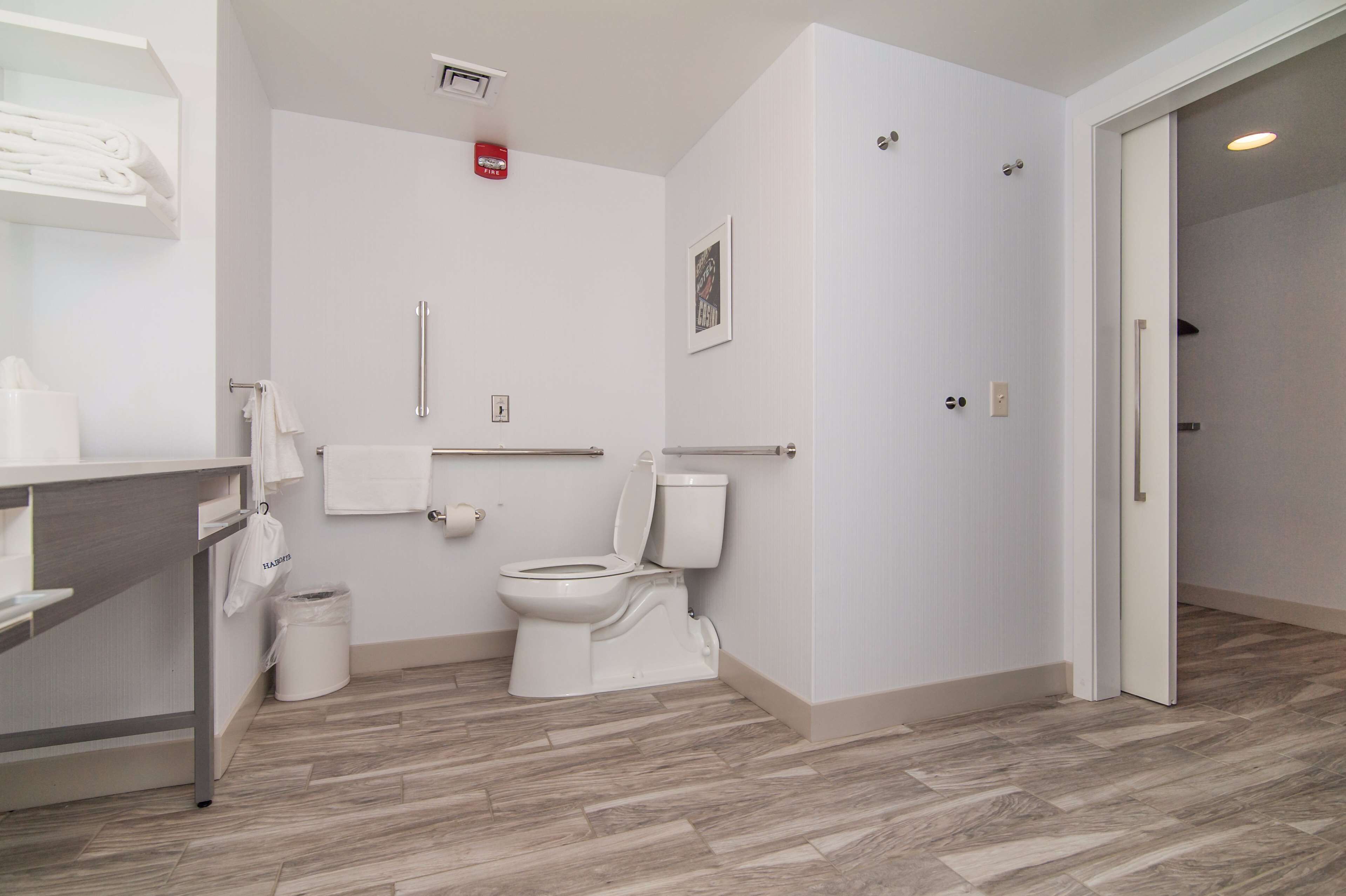 A modern bathroom with a toilet, a handrail, a towel rack, and a trash bin.