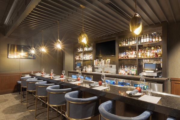 Zona de bar con una barra alargada, taburetes y estantes llenos de botellas.