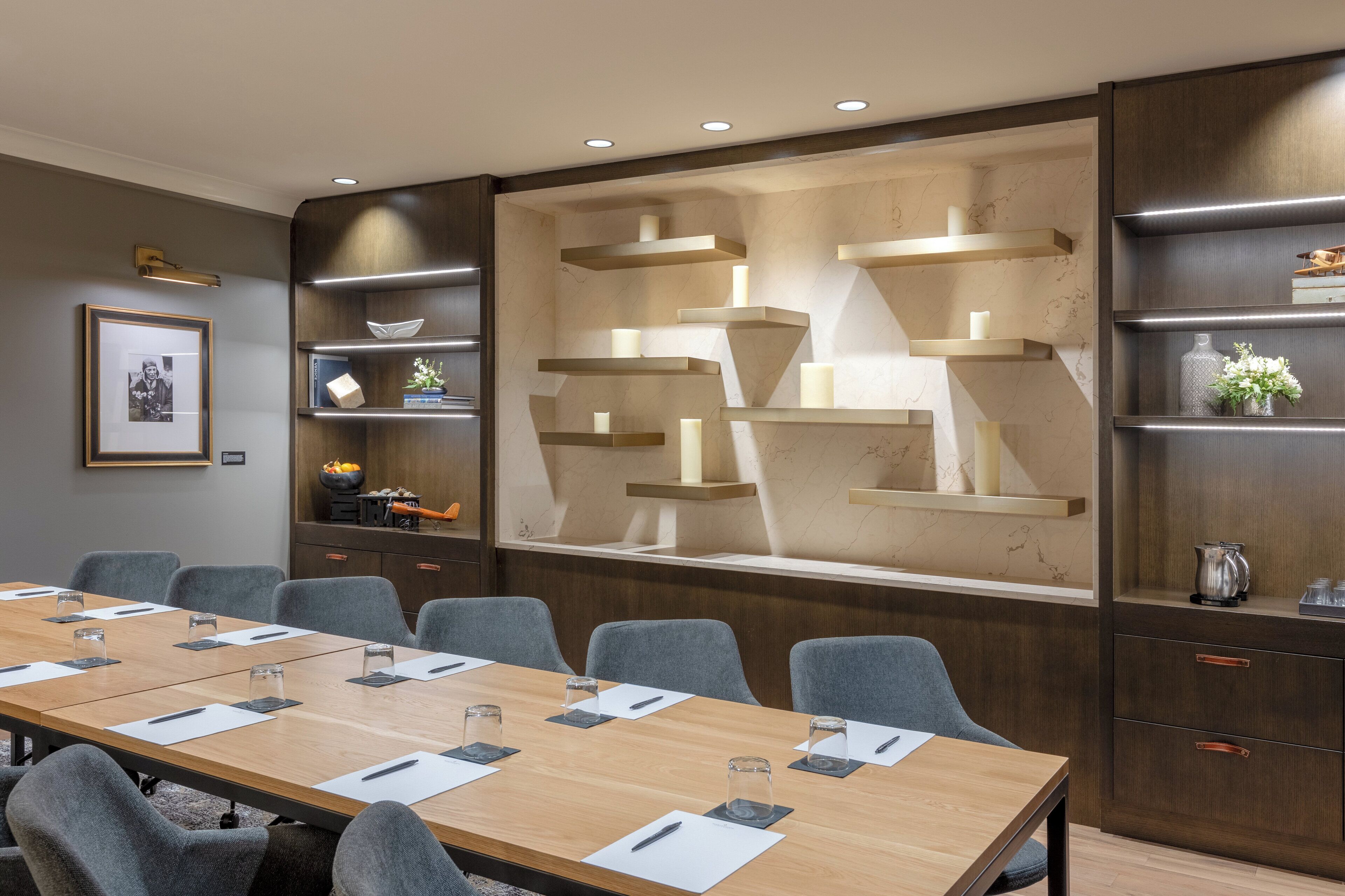 A conference room with a long table, grey chairs, and built-in shelving with decorative items.