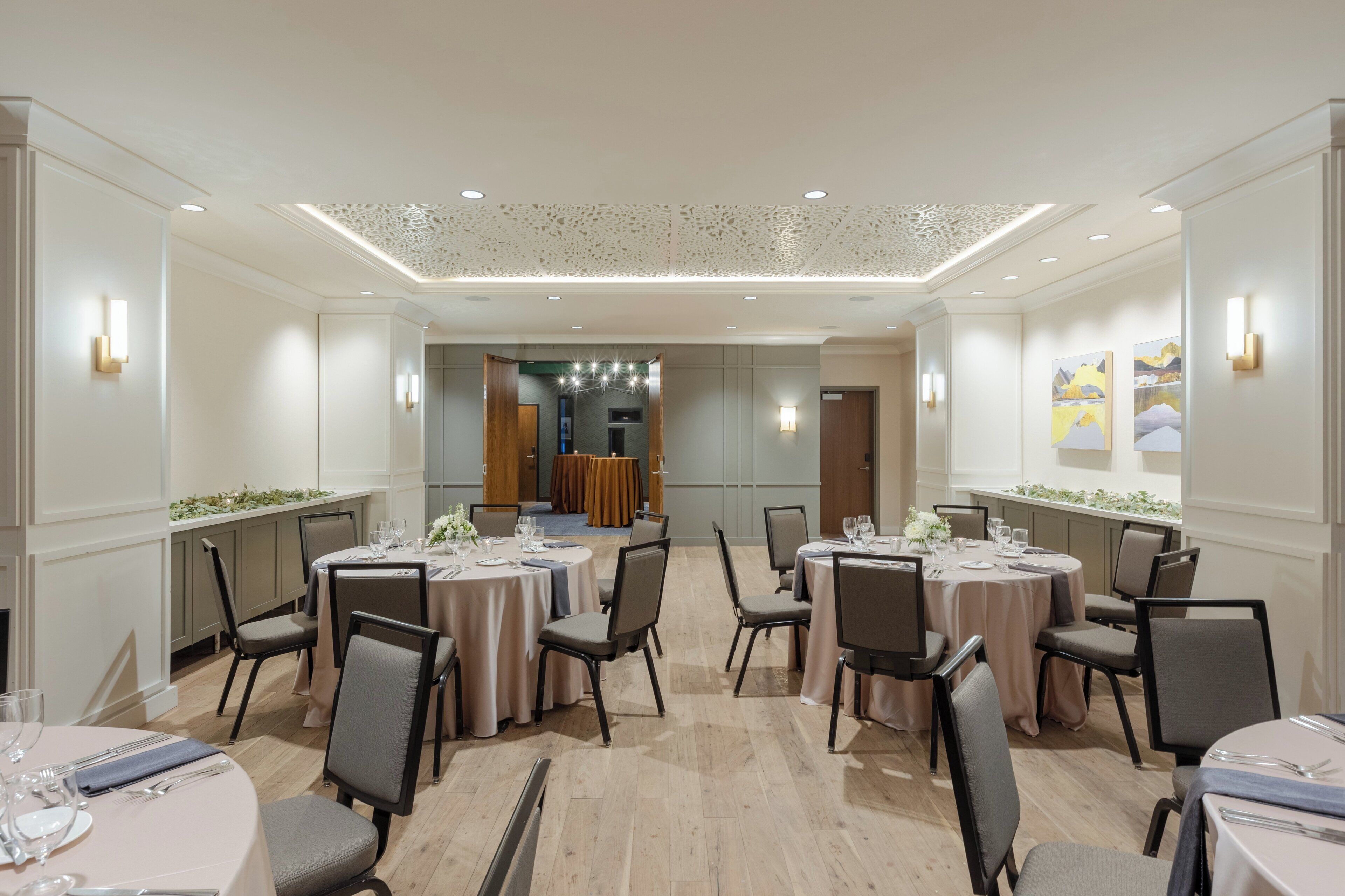 A spacious conference room with round tables and chairs, recessed lighting, and a decorative ceiling.