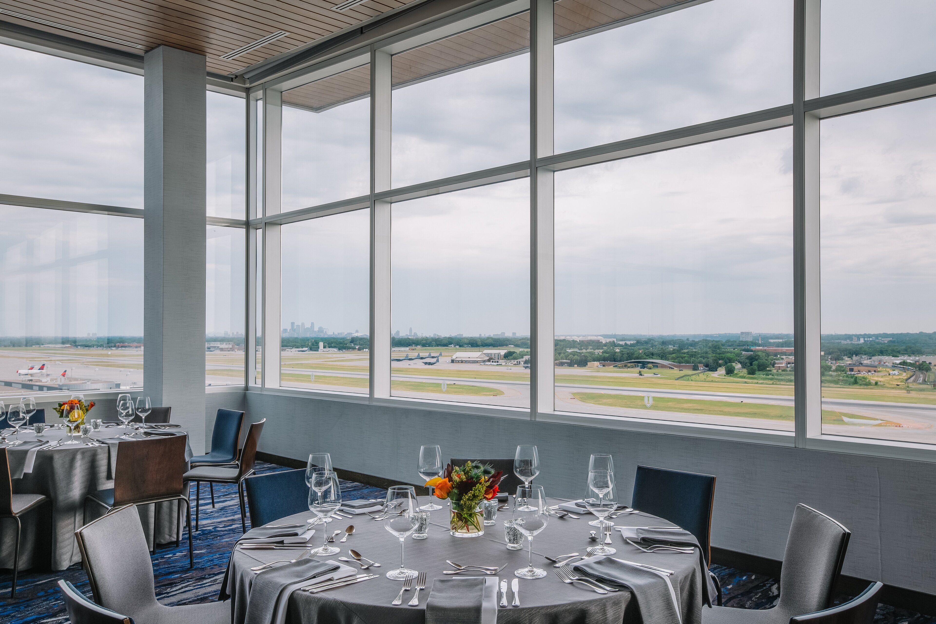 A dining area with tables set for a meal, large windows offering a view of an airport and cityscape.