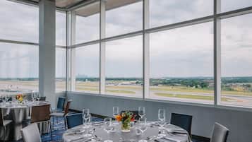 A dining area with tables set for a meal, large windows offering a view of an airport and cityscape.