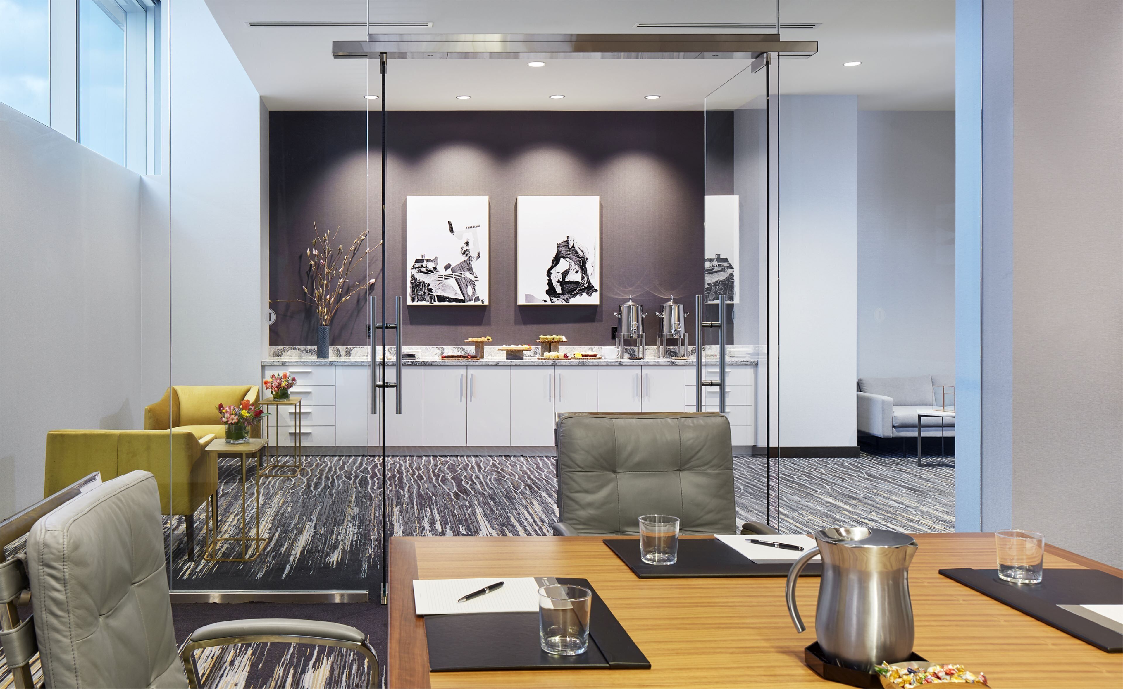 A modern conference room with a glass partition, a wooden table, and a coffee pot.
