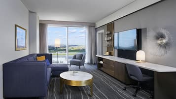 Una habitación de hotel moderna con sofá, sillón, escritorio y un televisor grande.