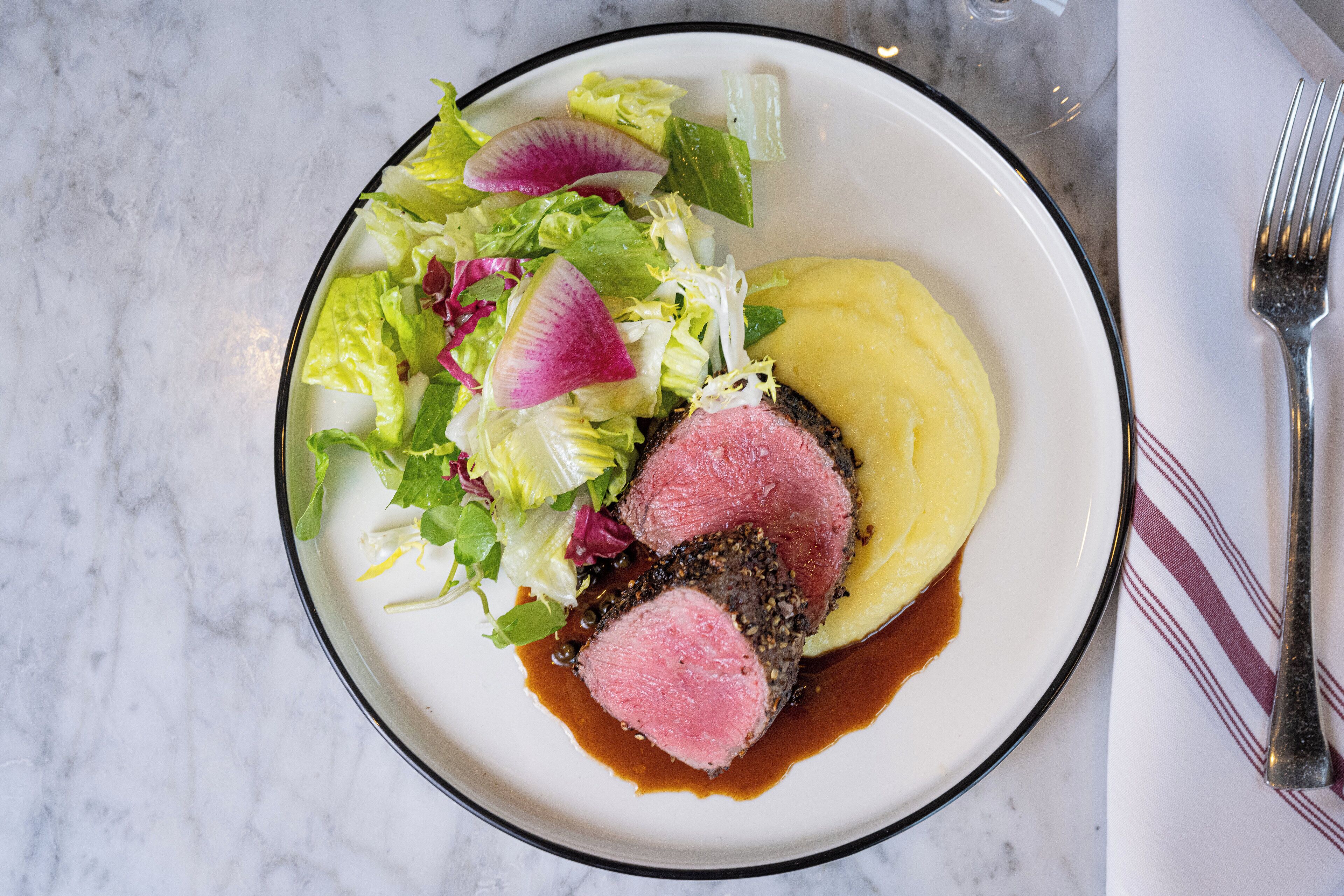 A plate with a steak, mashed potatoes, and a salad.