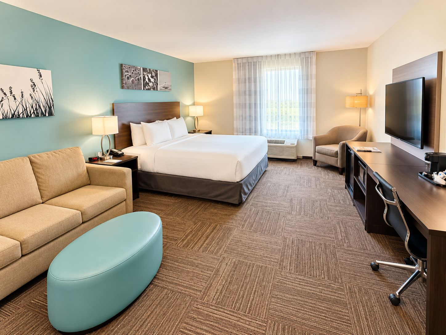 Una habitación de hotel con cama, sofá, escritorio, silla, televisión y obras de arte en las paredes.