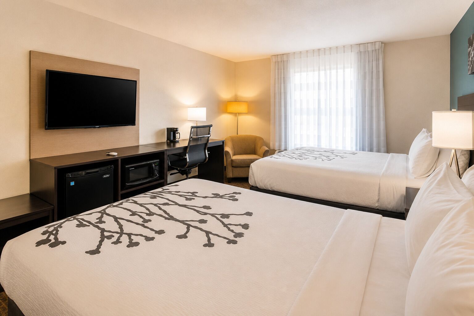 Una camera d'albergo con due letti, una scrivania con televisore a schermo piatto, una macchina per il caffè, una lampada e una sedia.