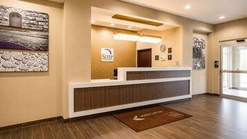 A hotel reception area with a reception desk, a clock, and a welcome mat.