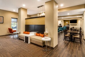 A hotel lobby with a seating area, a small table with a drink dispenser, and a dining area with multiple tables and chairs.