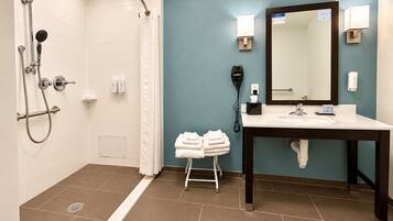 Un baño con ducha, lavamanos, espejo y toallero.