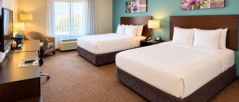 A hotel room with two beds, a desk, a chair, a lamp, and artwork on the walls.