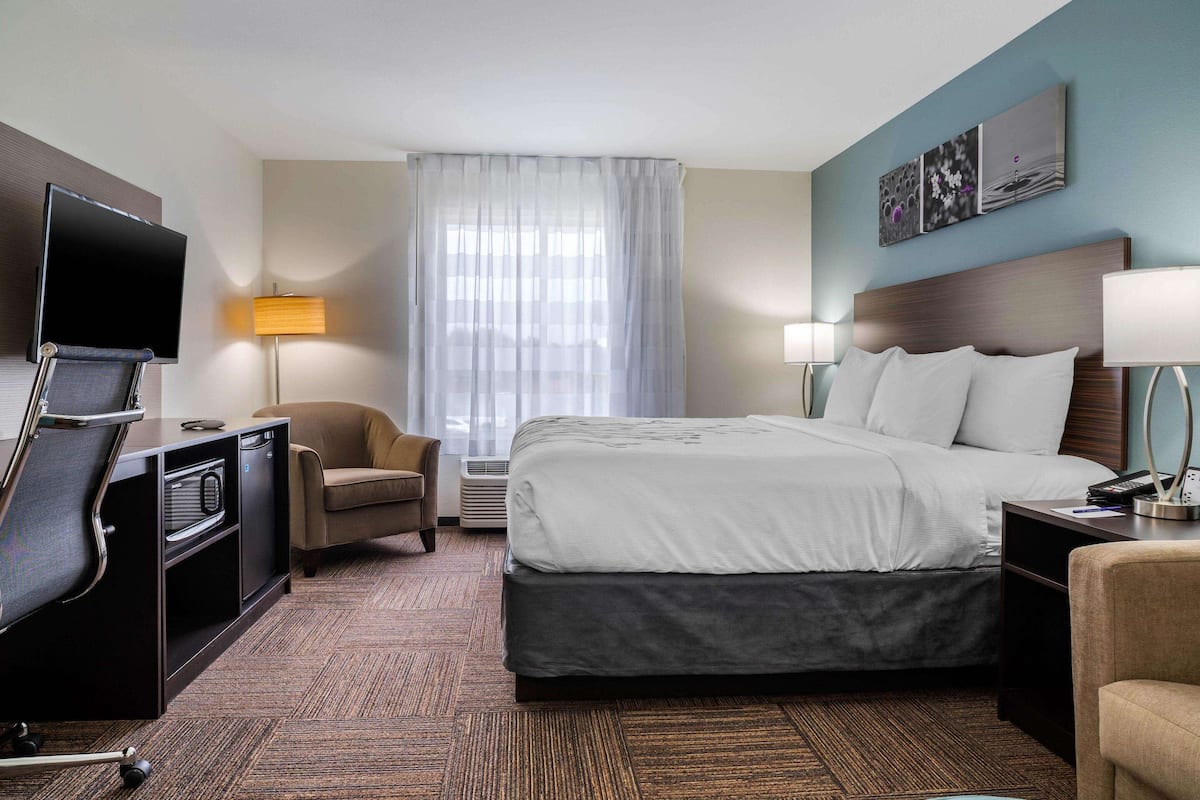 A hotel room with a bed, a desk with a computer, a chair, a TV, and a lamp.