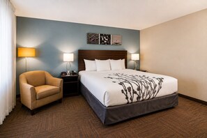 A hotel room with a bed, a chair, two bedside tables with lamps, and a wall with artwork. - Sleep Inn & Suites Houston Westchase - Little Saigon (Houston)