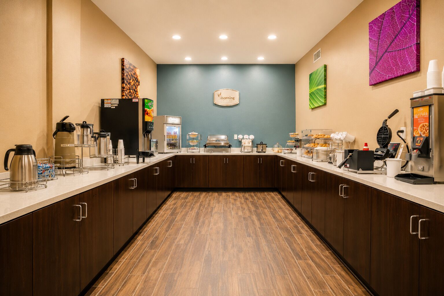A hotel kitchen with a breakfast bar, coffee machines, and a clock on the wall.