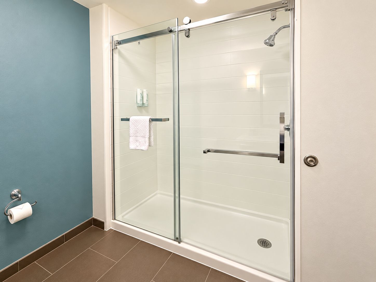 A glass-enclosed shower with a towel rack, a toilet paper holder, and a showerhead.