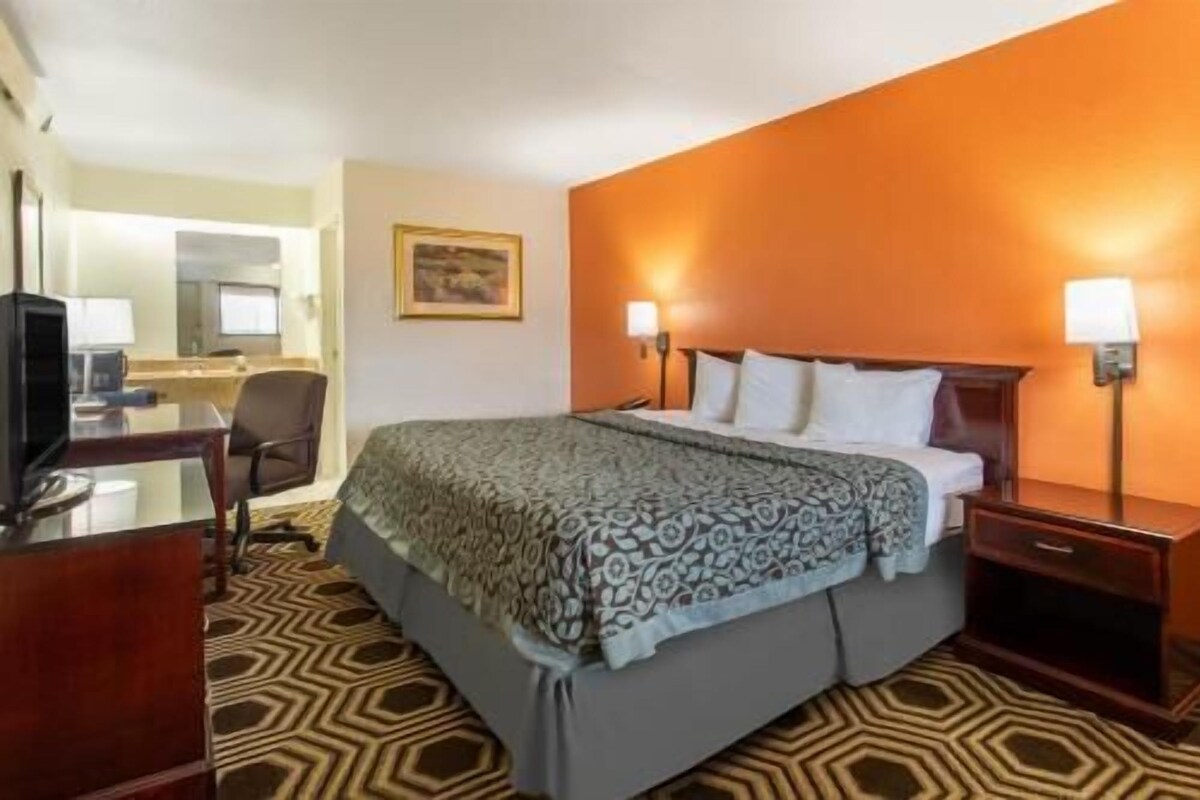 A hotel room with a bed, bedside tables, a desk with a chair, a television, and a mirror.