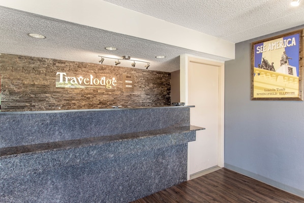 Un mostrador de recepción con un fondo de pared de piedra y un cartel de 'Travelodge'.