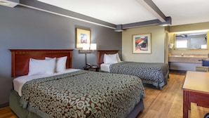 Ett hotellrum med två sängar, ett trägolv, ett skrivbord och ett badrum med en spegel.
