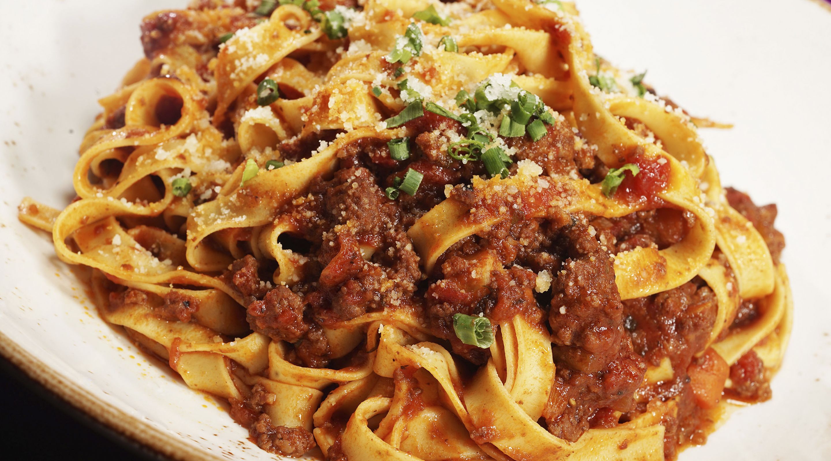 A plate of pasta with a meat sauce, garnished with grated cheese and chopped green onions.