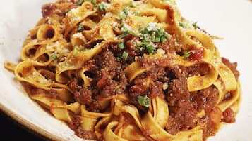 Un plato de pasta con salsa de carne, adornado con queso rallado y cebollín picado.