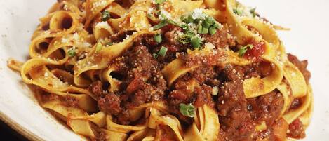 Un plato de pasta con salsa de carne, adornado con queso rallado y cebollín picado.