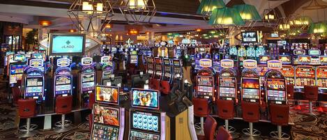 A casino with multiple slot machines and red bar chairs.