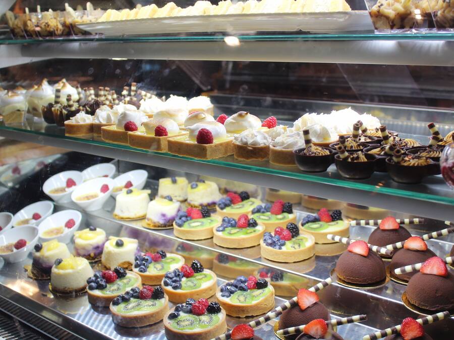 Una vitrina exhibe diversos postres, entre ellos pasteles y productos de pastelería, dispuestos en varias estanterías.