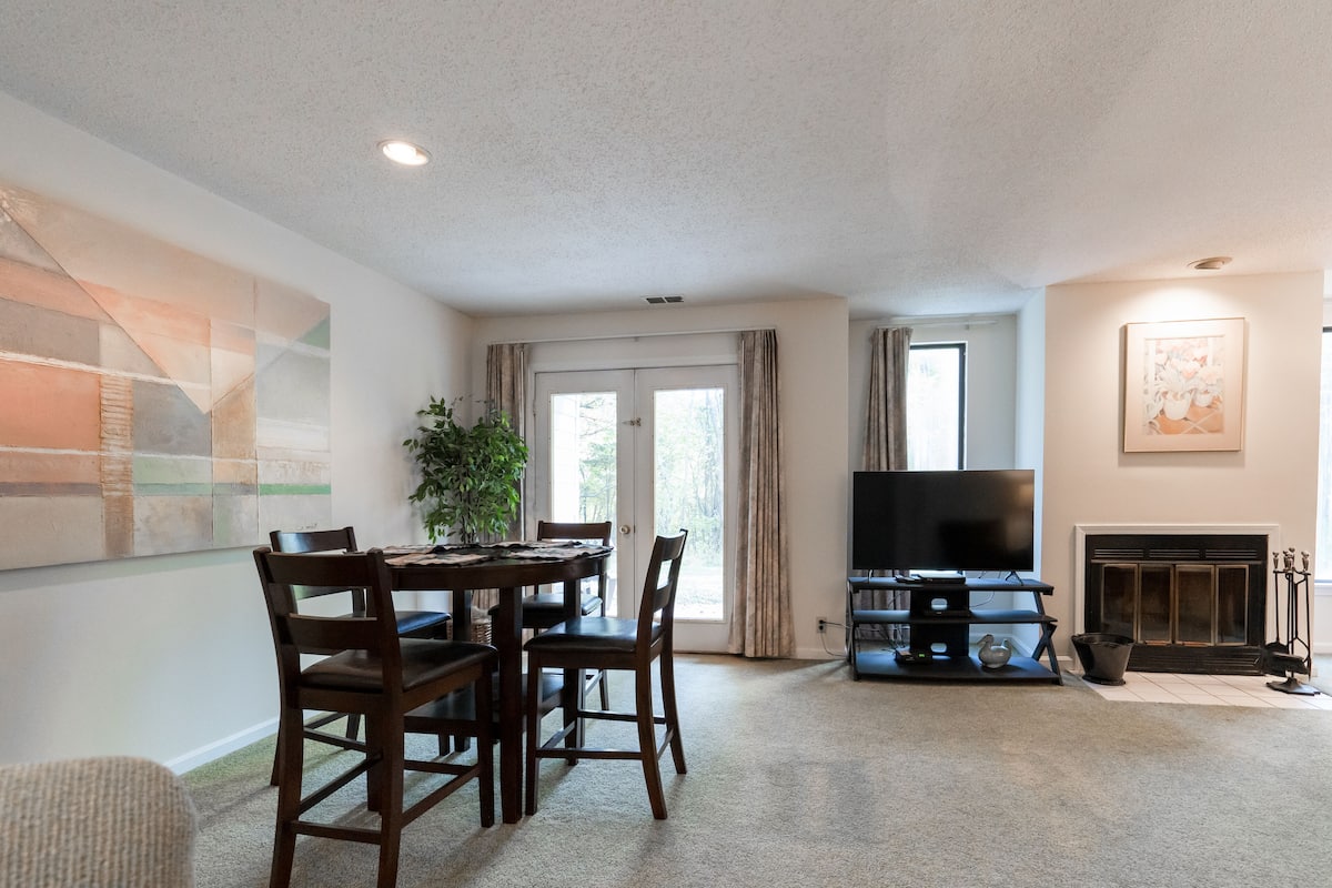 A living room with a dining table, chairs, a flat-screen TV, a fireplace, and a large abstract painting on the wall.