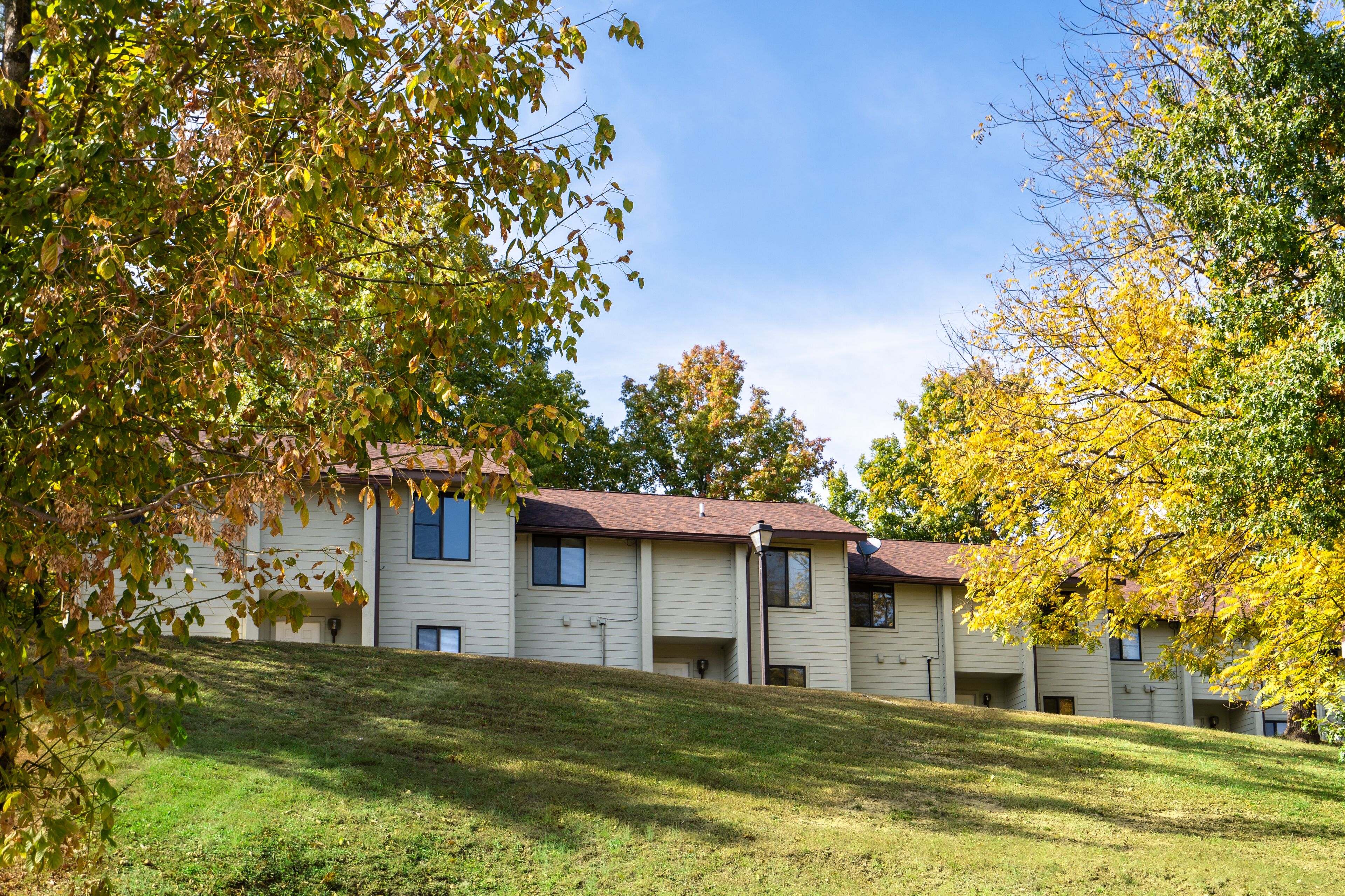 A row of two-story buildings with a sloped roof, surrounded by trees with autumn foliage.