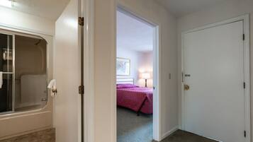 Una habitación con una bañera, una cama con cubrecama rosa y una puerta que da a otra habitación.